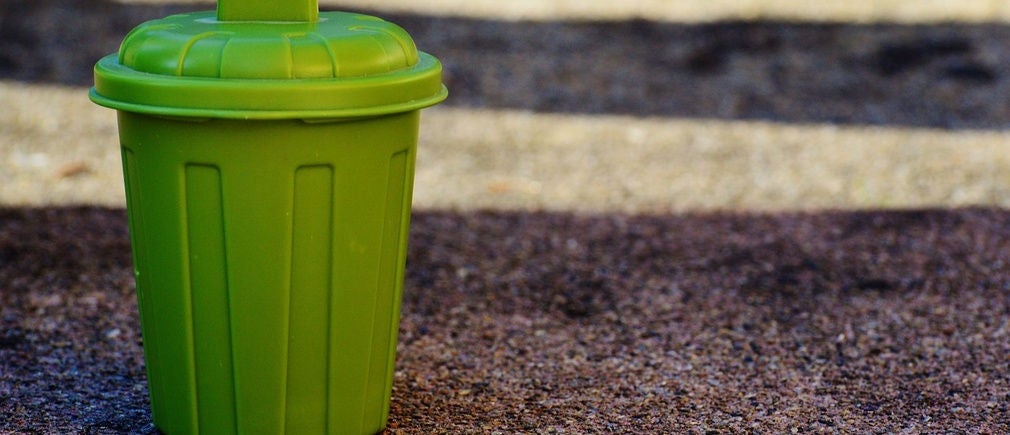 Une petite poubelle verte posée sur un trottoir