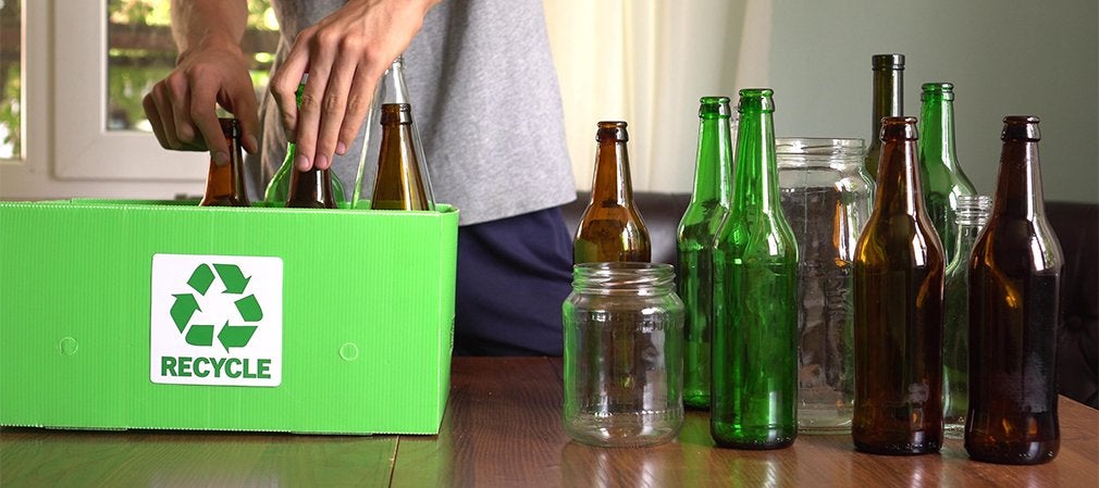 Personne déposant des bouteilles en verre dans une boîte de recyclage verte