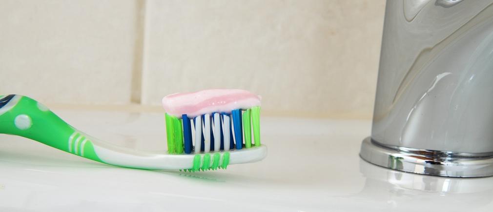 Dentifrice rose déposé sur une brosse à dents verte