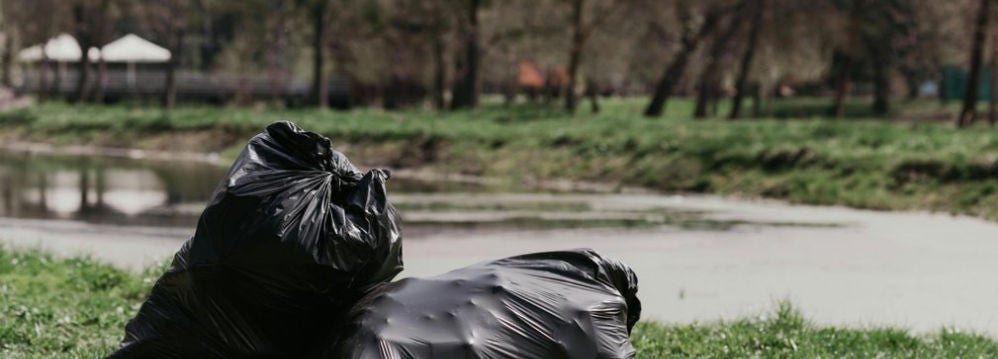 Deux sacs poubelle noirs poses sur l'herbe au bord d'un etang calme