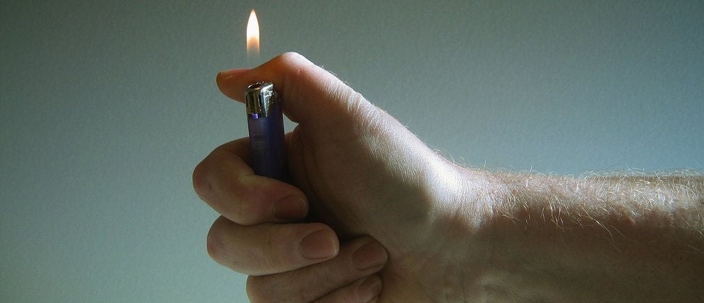 Main tenant un briquet allumé sur fond gris