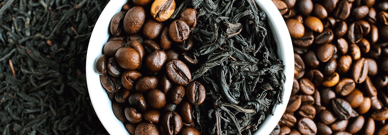 Un bol blanc contenant des grains de café et des feuilles de thé, posé sur un lit de grains de café, illustrant le recyclage et la valorisation des produits du café et du thé 