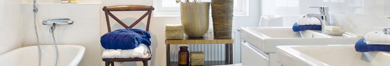 Baño moderno con lavabos dobles, toallas dobladas en una silla y plantas decorativas