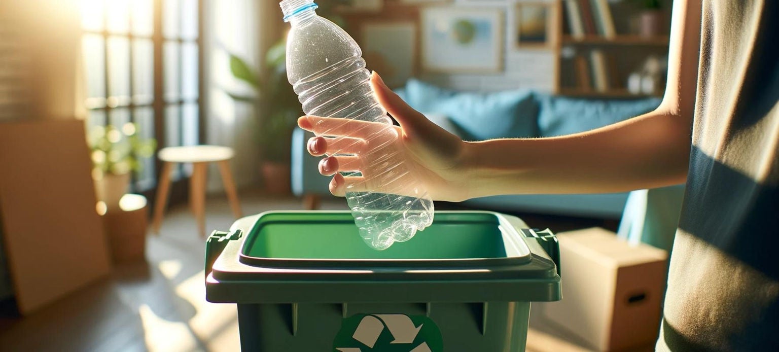 Une main tient une bouteille plastique au-dessus d’un bac de recyclage